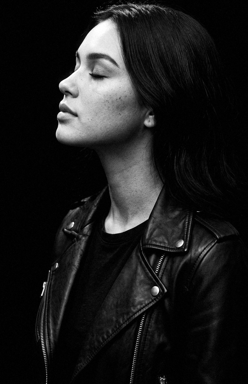 Nova Rai in profile under a single light with her eyes closed, in black and white