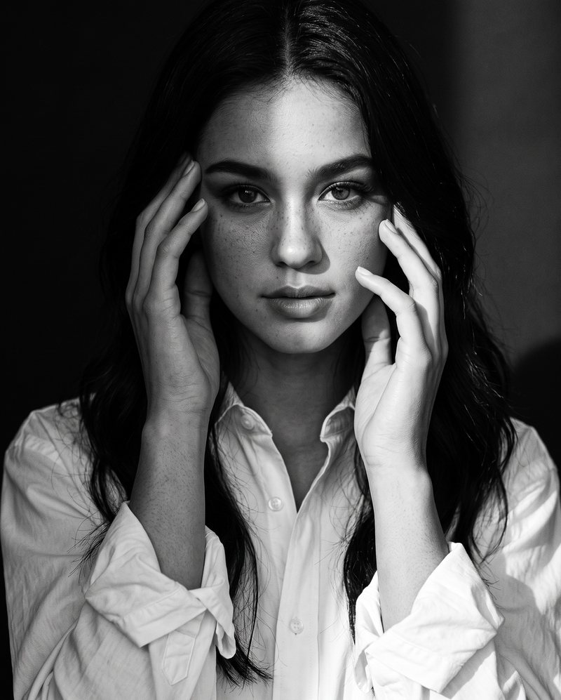 Nova Rai with her hands in her hair, looking straight at the camera, in black and white