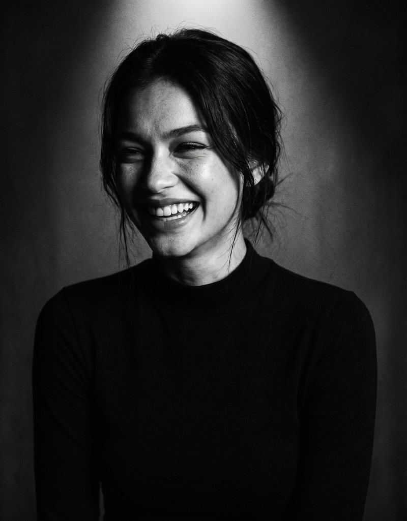 Nova Rai laughing between takes under a single light, in black and white
