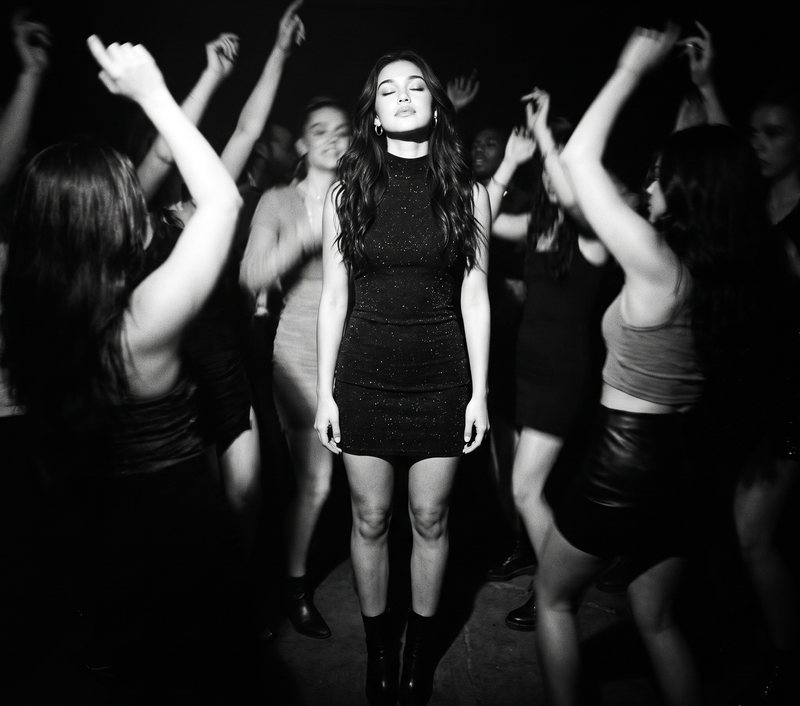 Nova Rai standing in the middle of a dancing crowd, in black and white